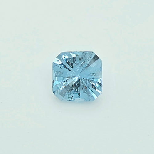 A single light blue square-cut gemstone, centered on a clean, pale off-white background.