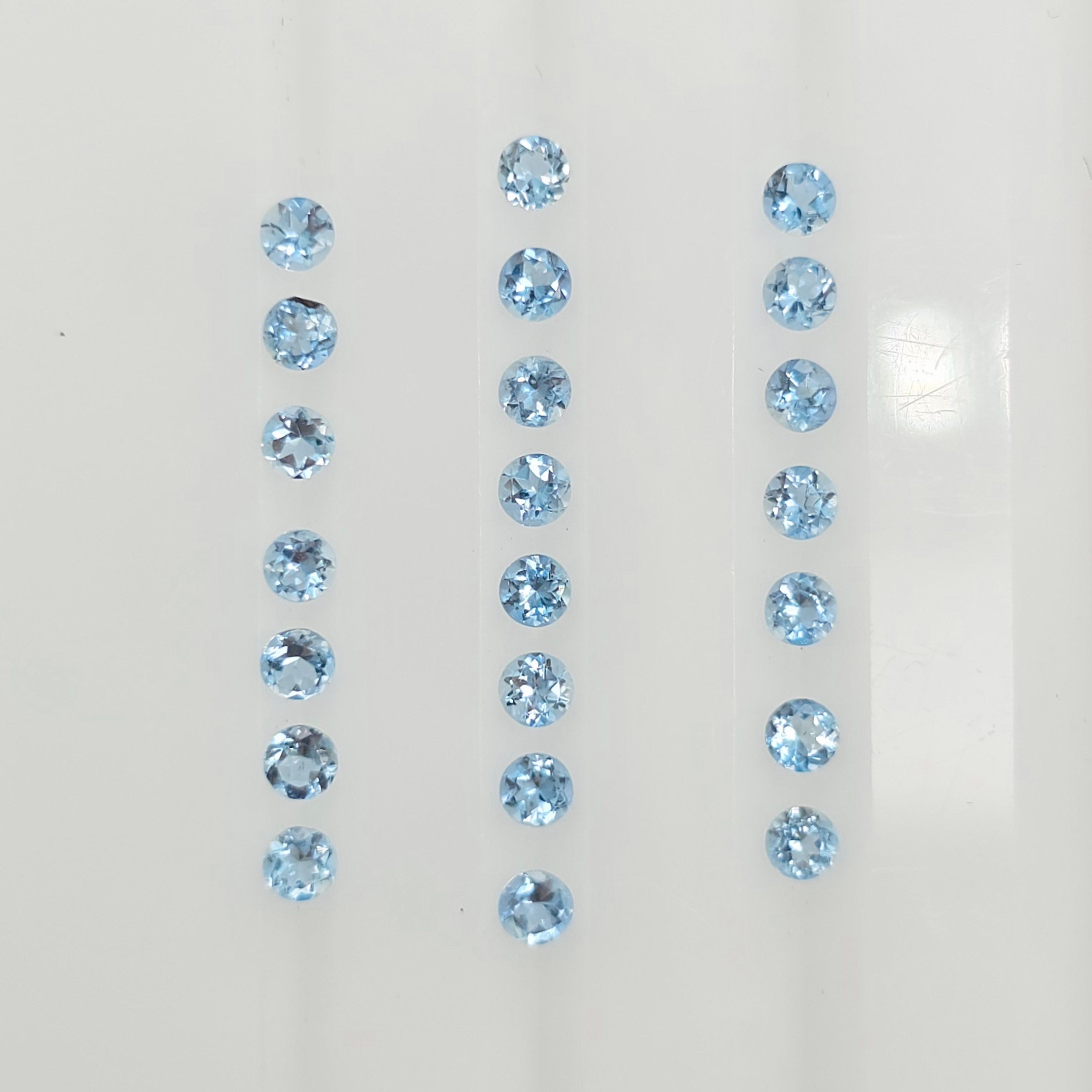 22 light blue round faceted blue gemstones arranged in three vertical columns on a plain white background.