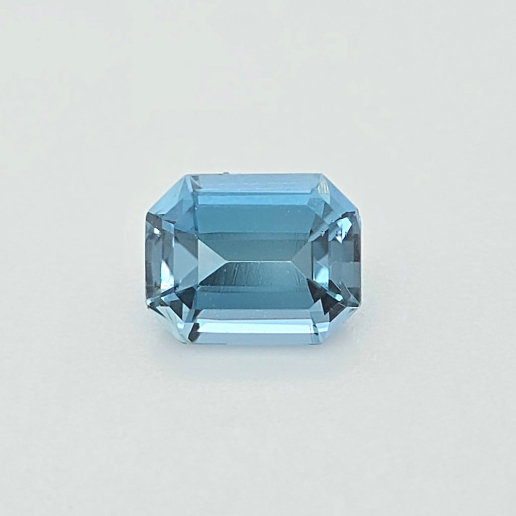 A light blue emerald-cut gemstone, centered on a clean, light gray background.
