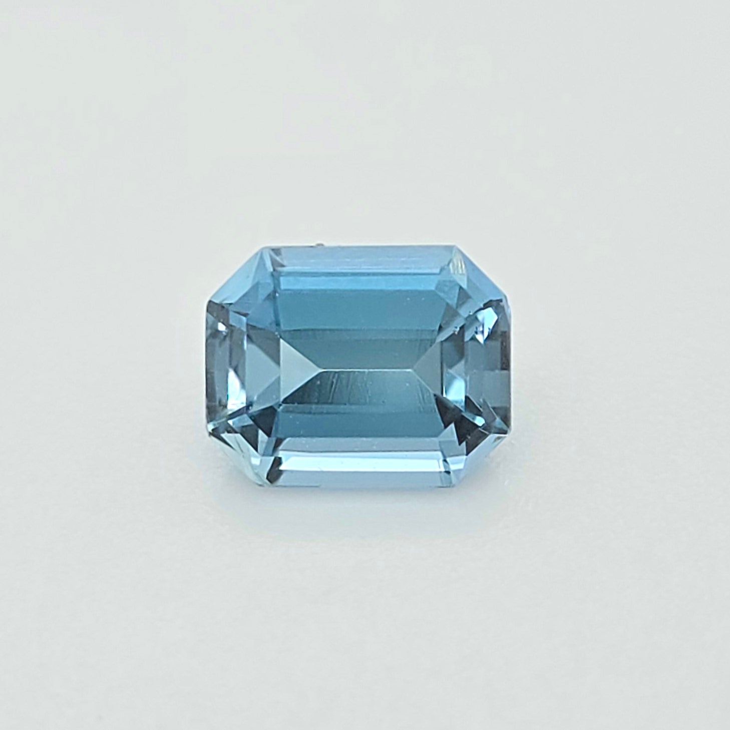 A light blue emerald-cut gemstone, centered on a clean, light gray background.