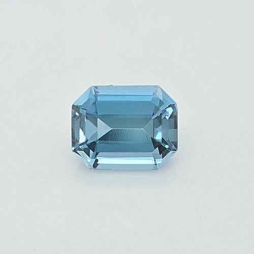 A light blue emerald-cut gemstone, centered on a clean, light gray background.