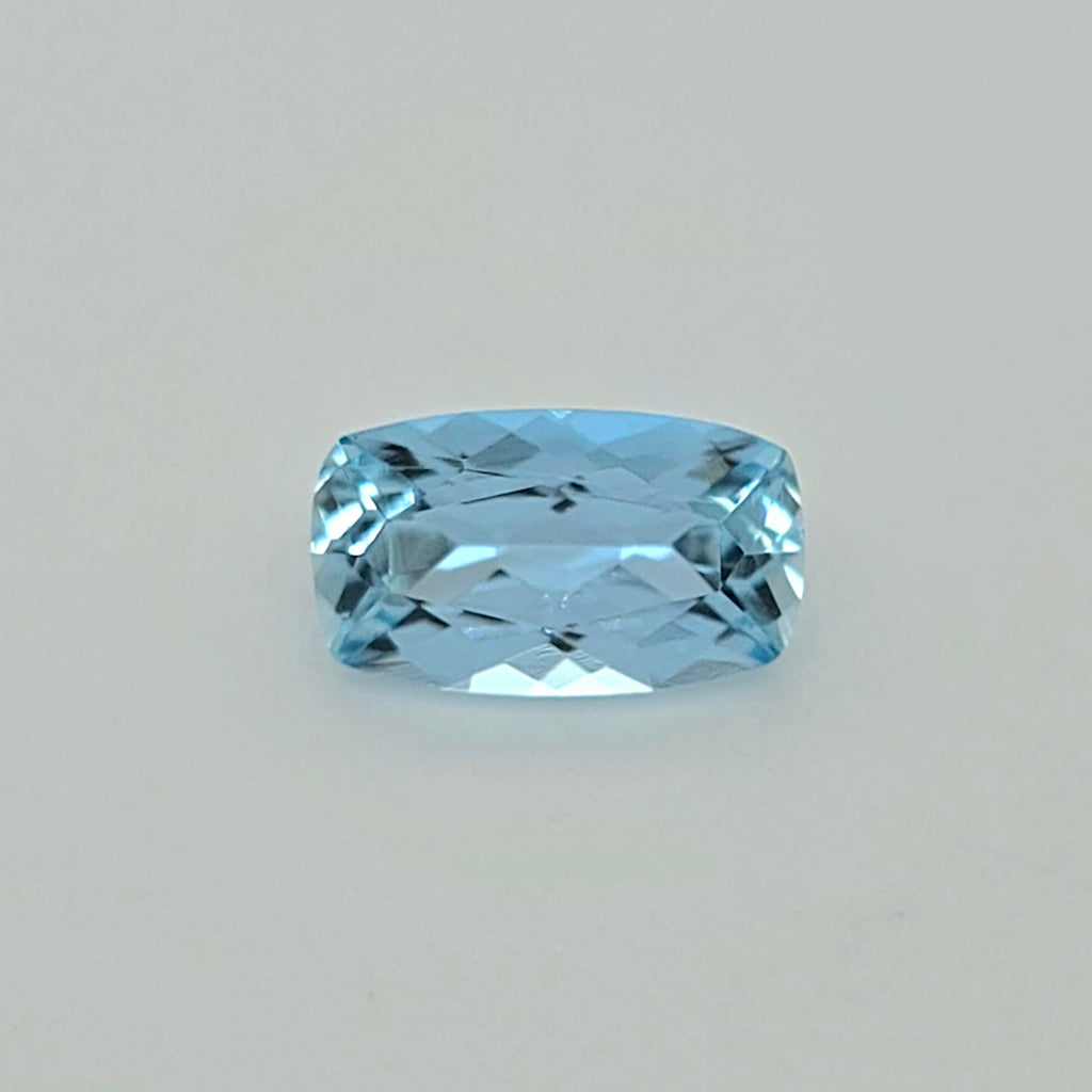 A light blue cushion-cut faceted gemstone centered on a plain light gray background.