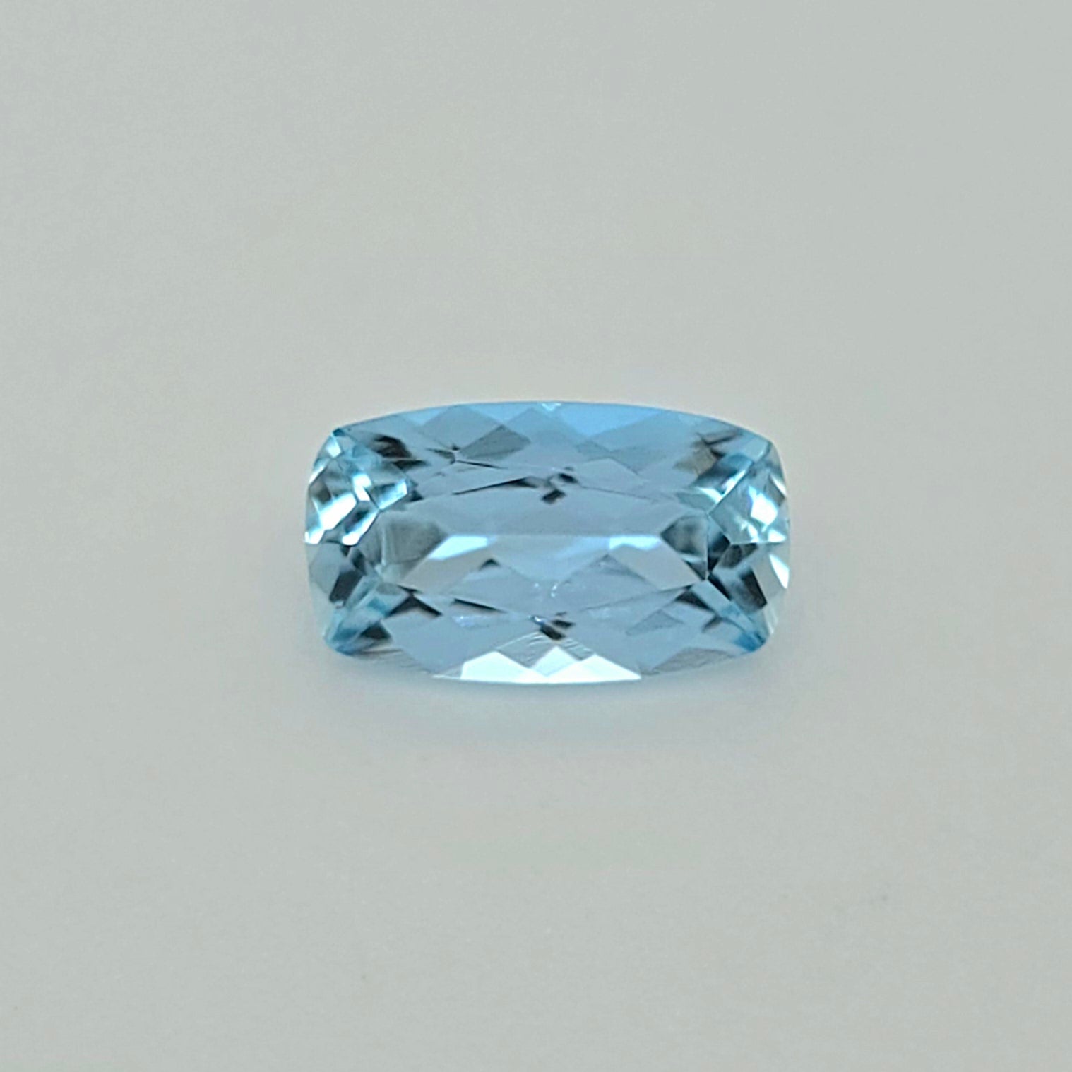 A light blue cushion-cut faceted gemstone centered on a plain light gray background.