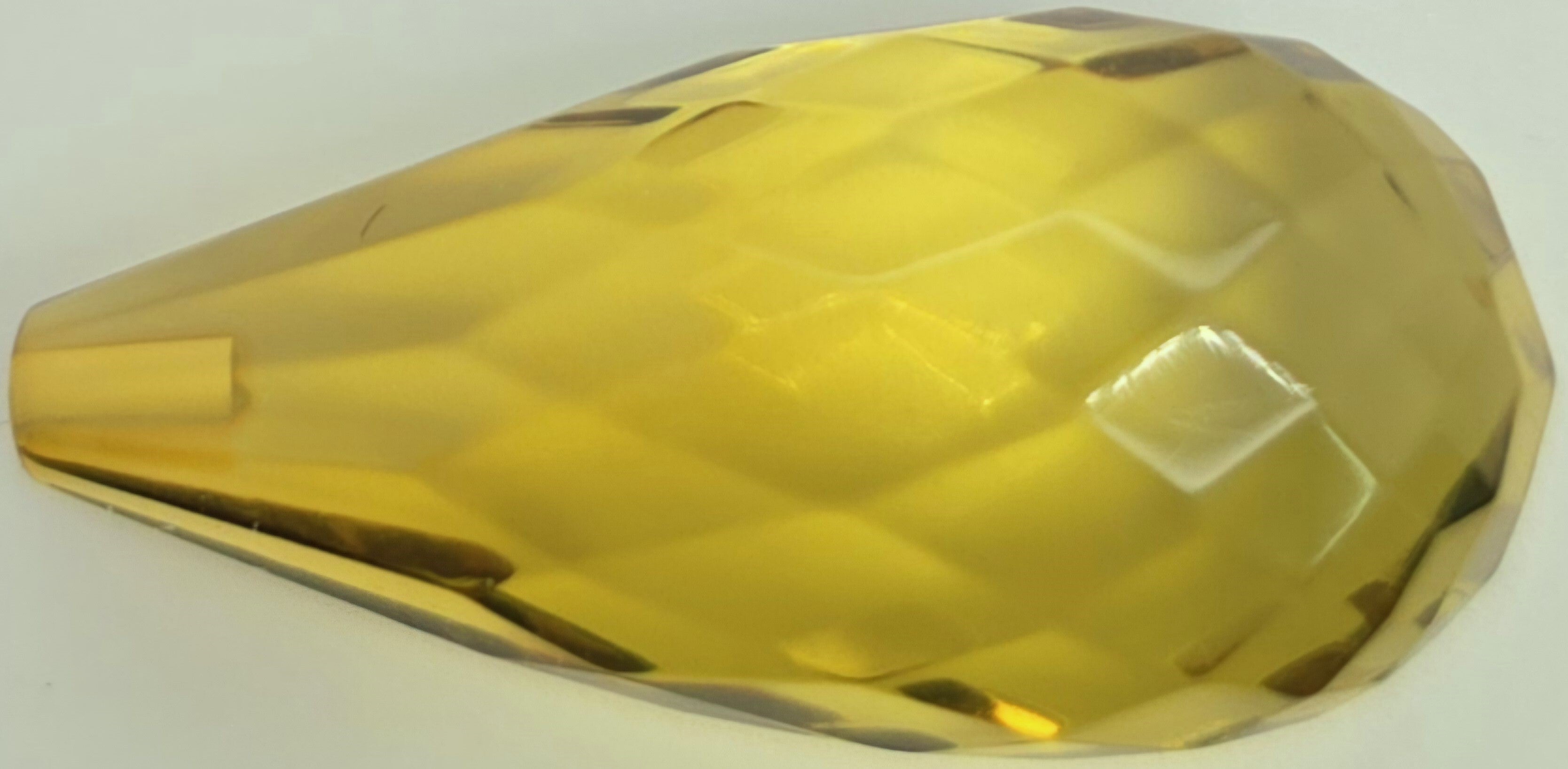 A faceted, teardrop-shaped transparent greenish yellow briolette on a plain white background.