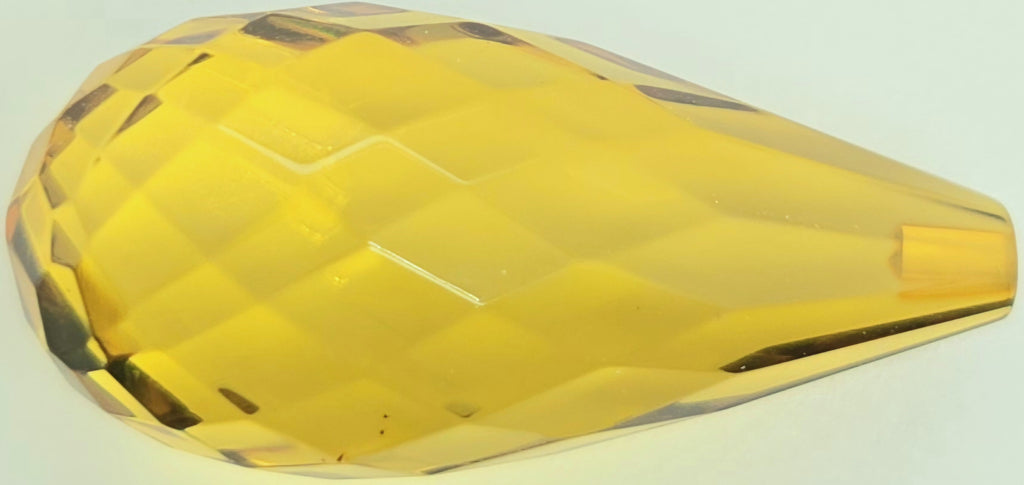 A faceted greenish yellow teardrop briolette on a plain white background.