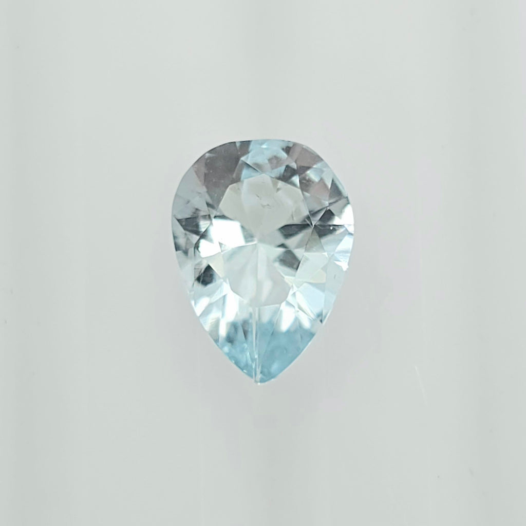 A single pear-cut light blue gemstone with a faceted, reflective surface, centered against a plain light gray background.