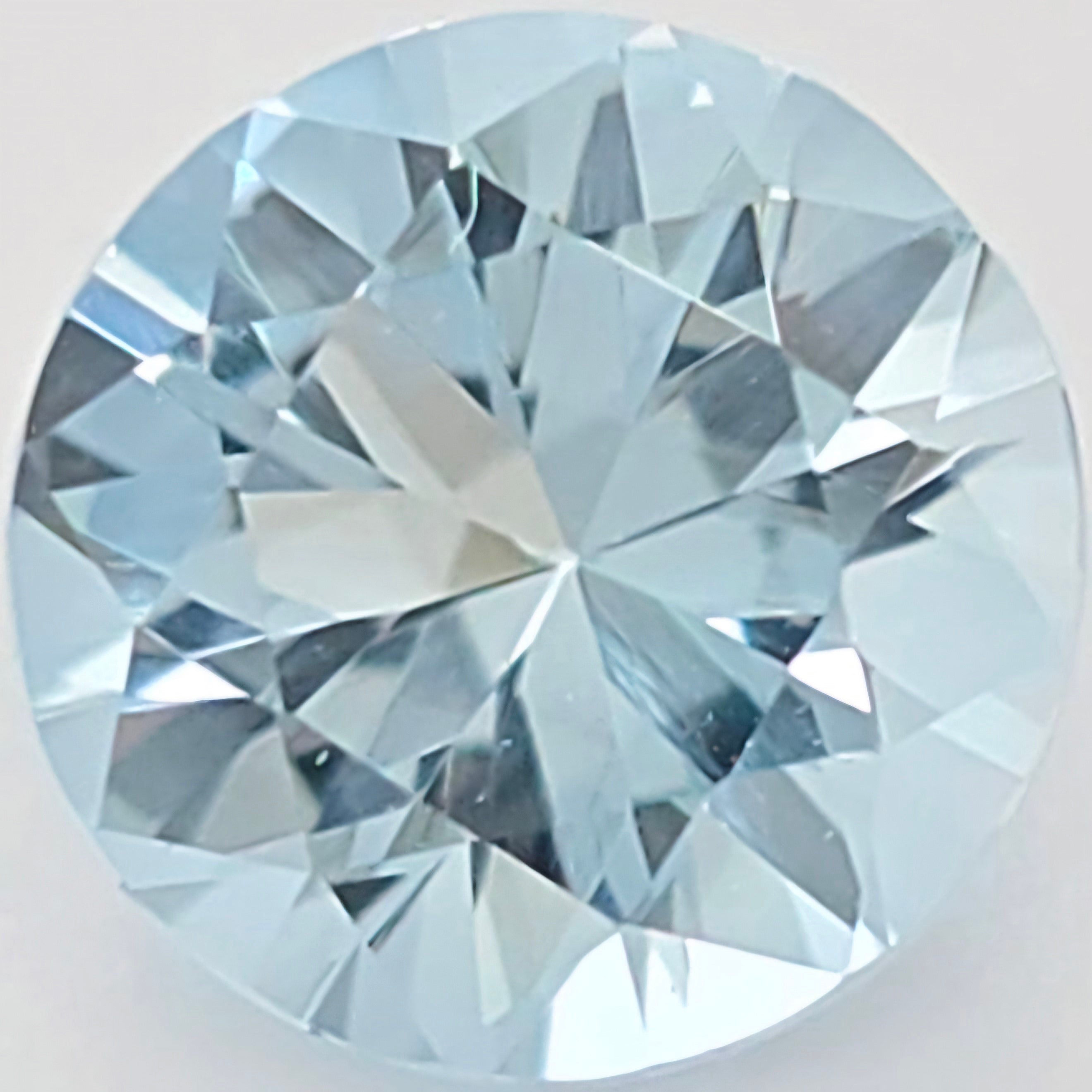 A round brilliant-cut light blue gemstone, showing detailed faceted reflections on a plain light background.
