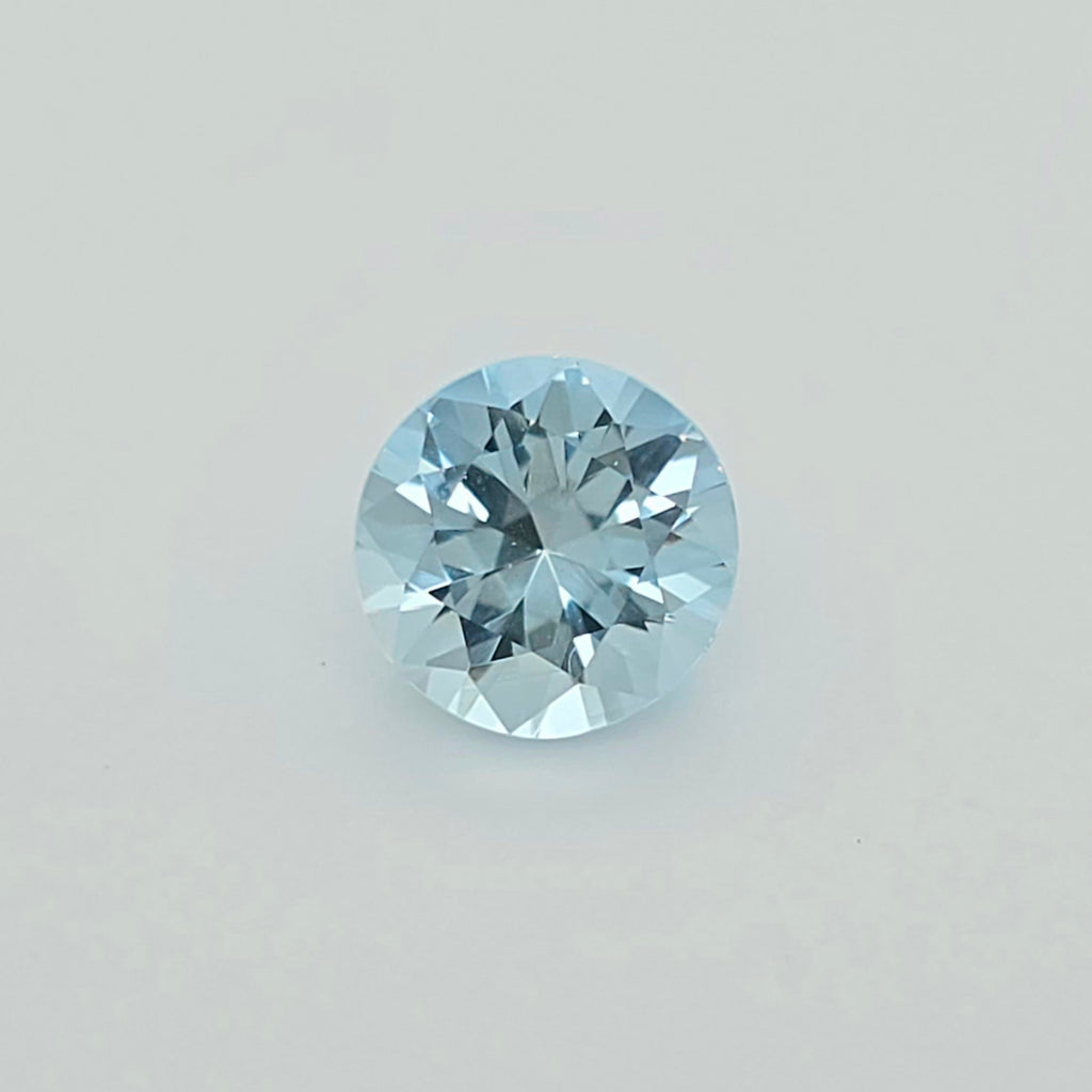 A round-cut light blue gemstone centered on a plain light gray background