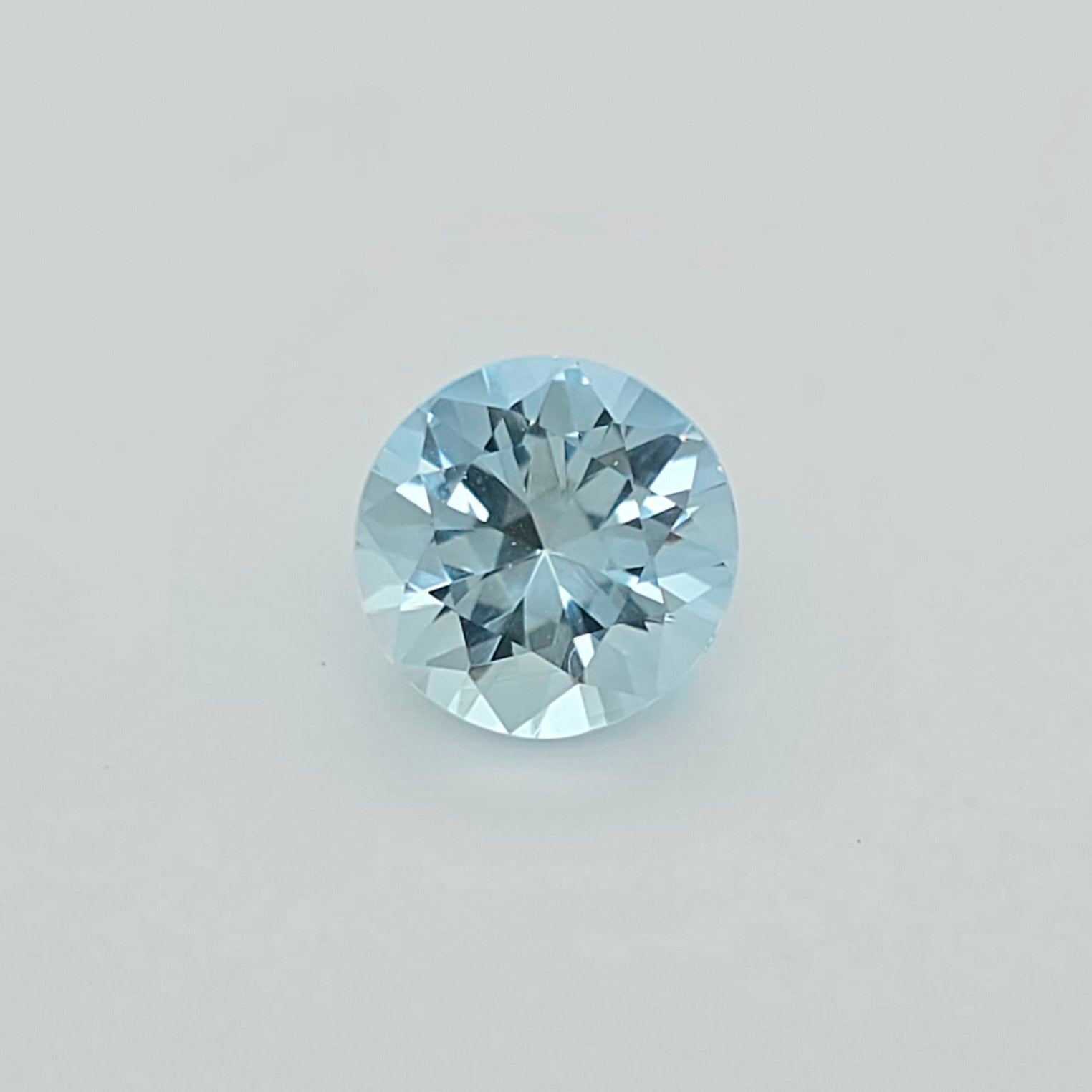 A round-cut light blue gemstone centered on a plain light gray background