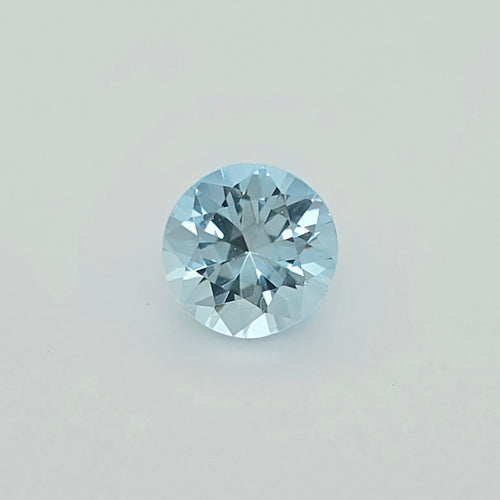 A round-cut light blue gemstone centered on a plain light gray background