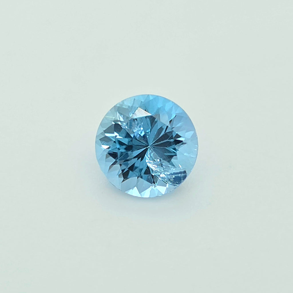A faceted round blue gemstone on a plain light background