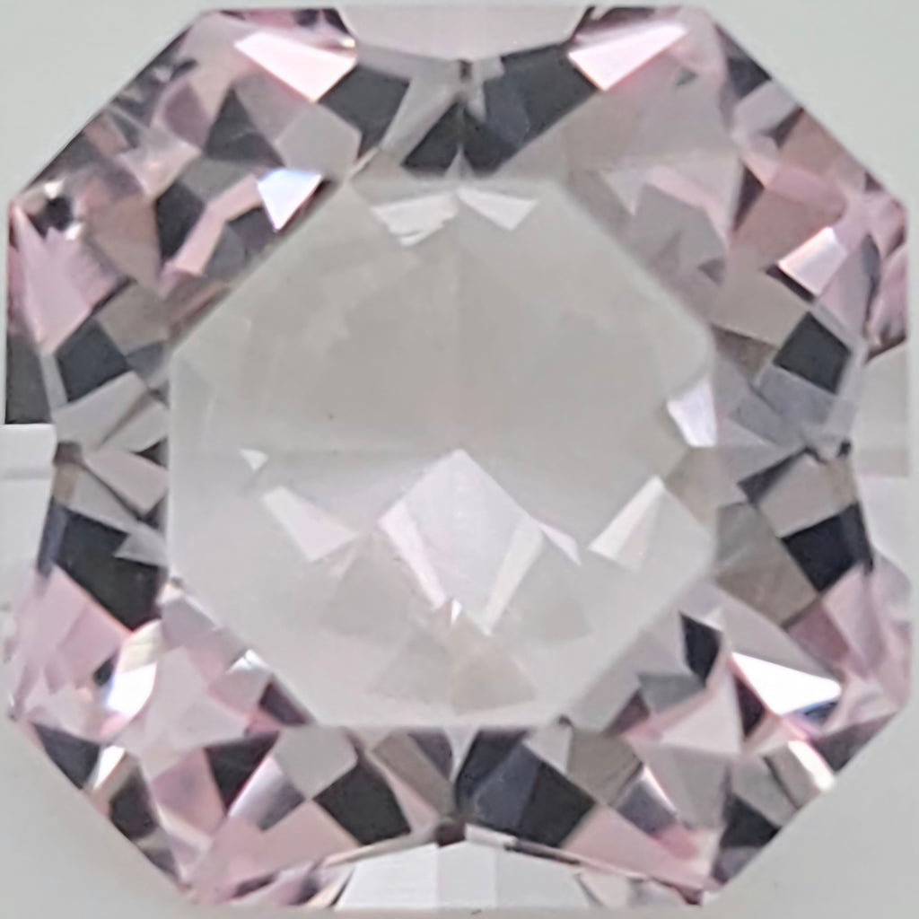 A close-up of a faceted pink gemstone with a clear center and light pink reflections around the edges.