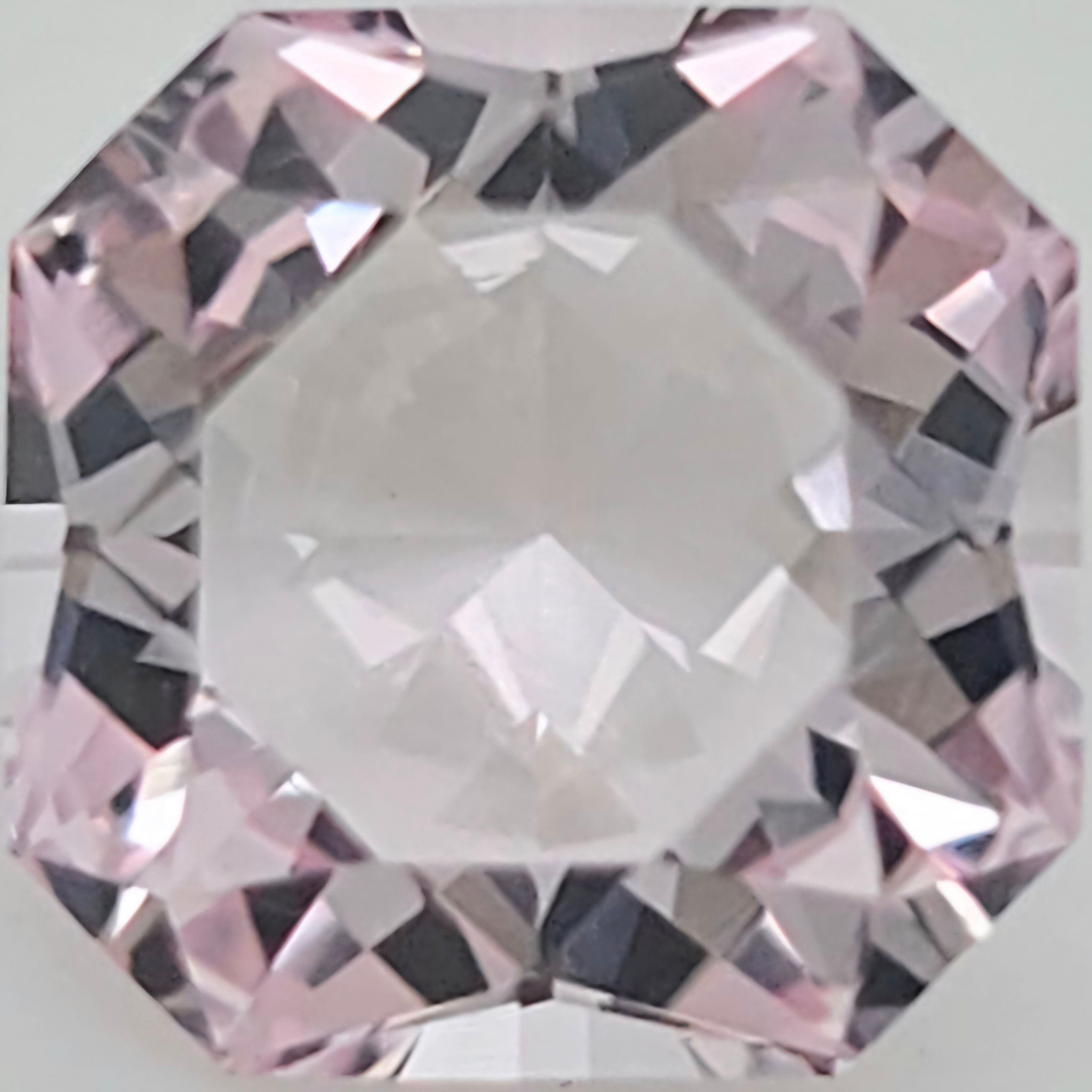 A close-up of a faceted pink gemstone with a clear center and light pink reflections around the edges.