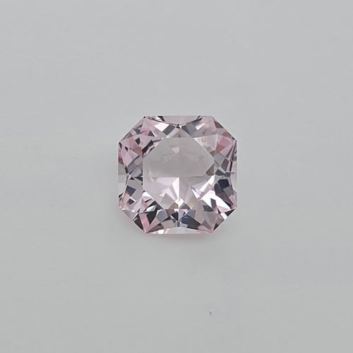 A single loose squaare radiant cut pink gemstone, centered on a plain light gray background.
