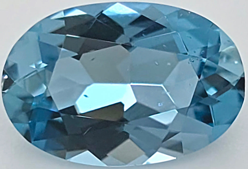 An oval-cut light blue faceted gemstone shown on a plain light gray background.