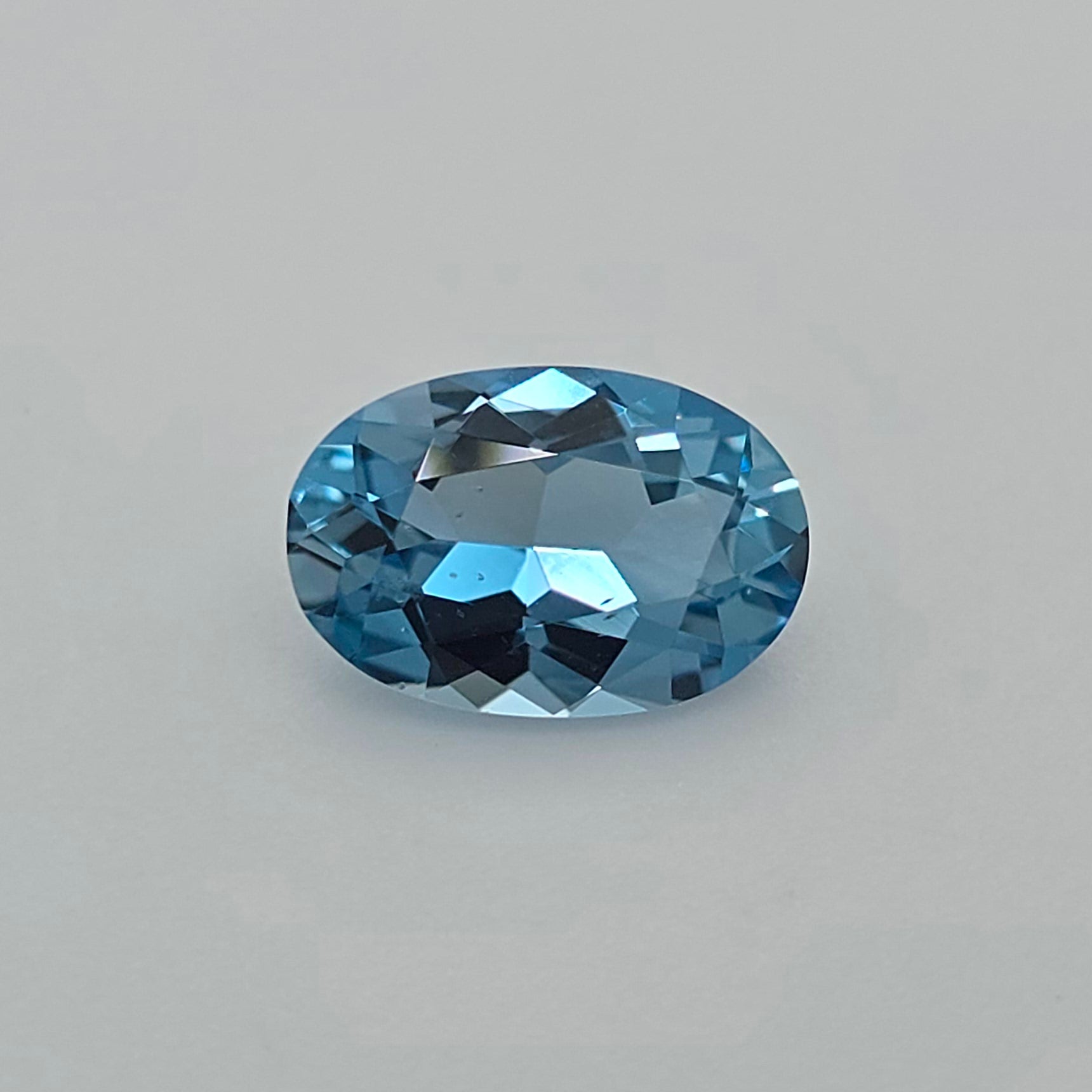 Faceted oval blue gemstone on a plain light gray background