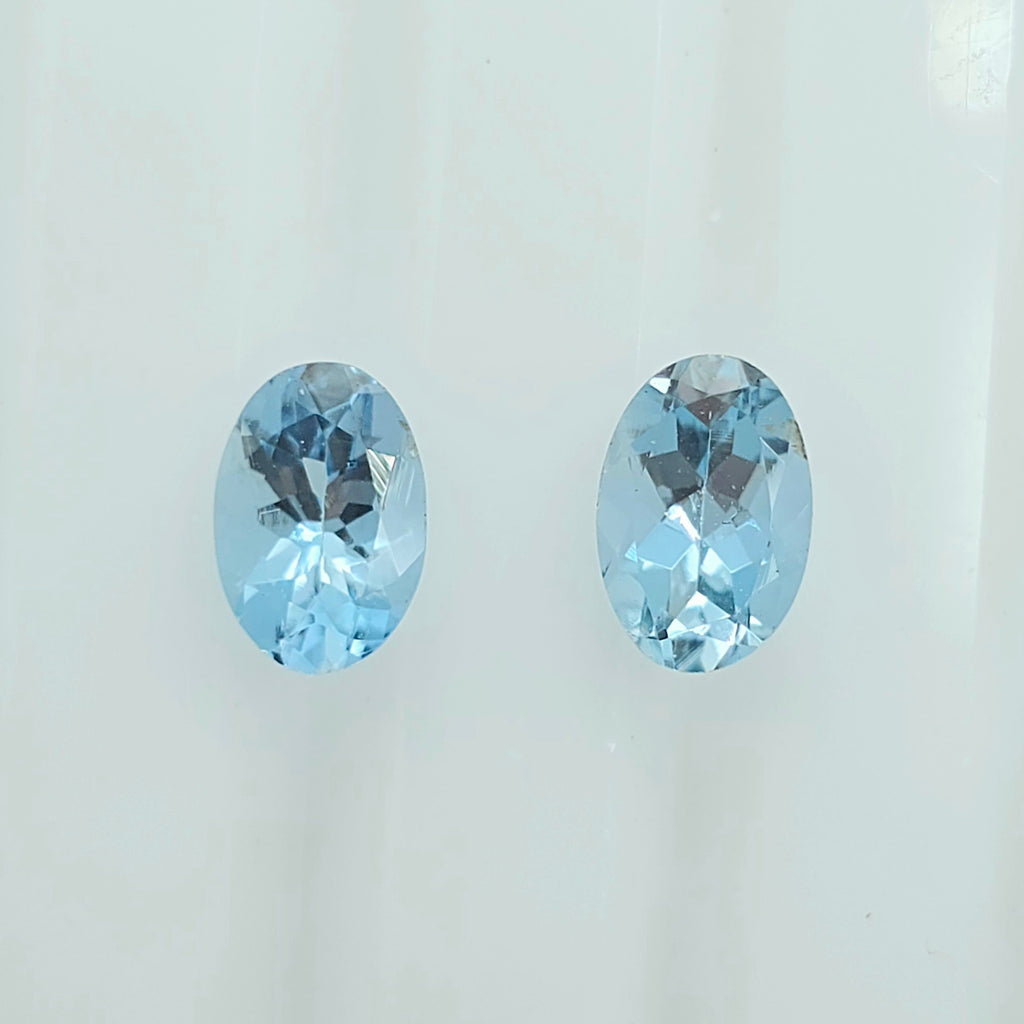 Two oval-cut light blue faceted gemstones displayed side by side on a plain white background.