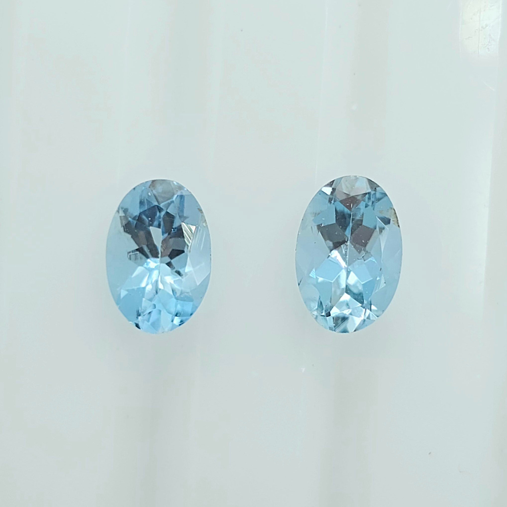 Two oval-cut light blue faceted gemstones displayed side by side on a plain white background.