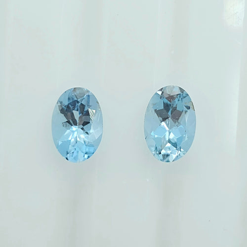 Two oval-cut light blue faceted gemstones displayed side by side on a plain white background.