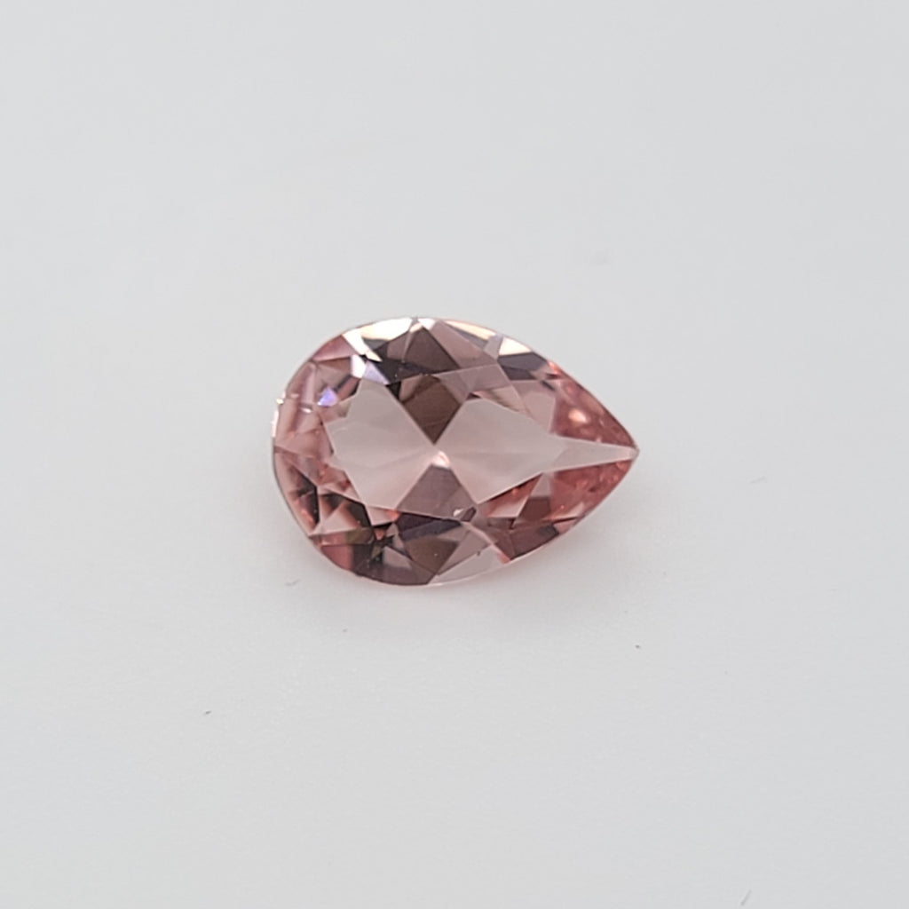Transparent pink pear shaped gemstone on a white background