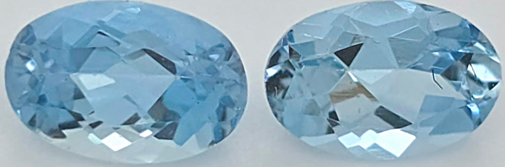 Two oval-cut light blue gemstones shown side by side on a plain light background.