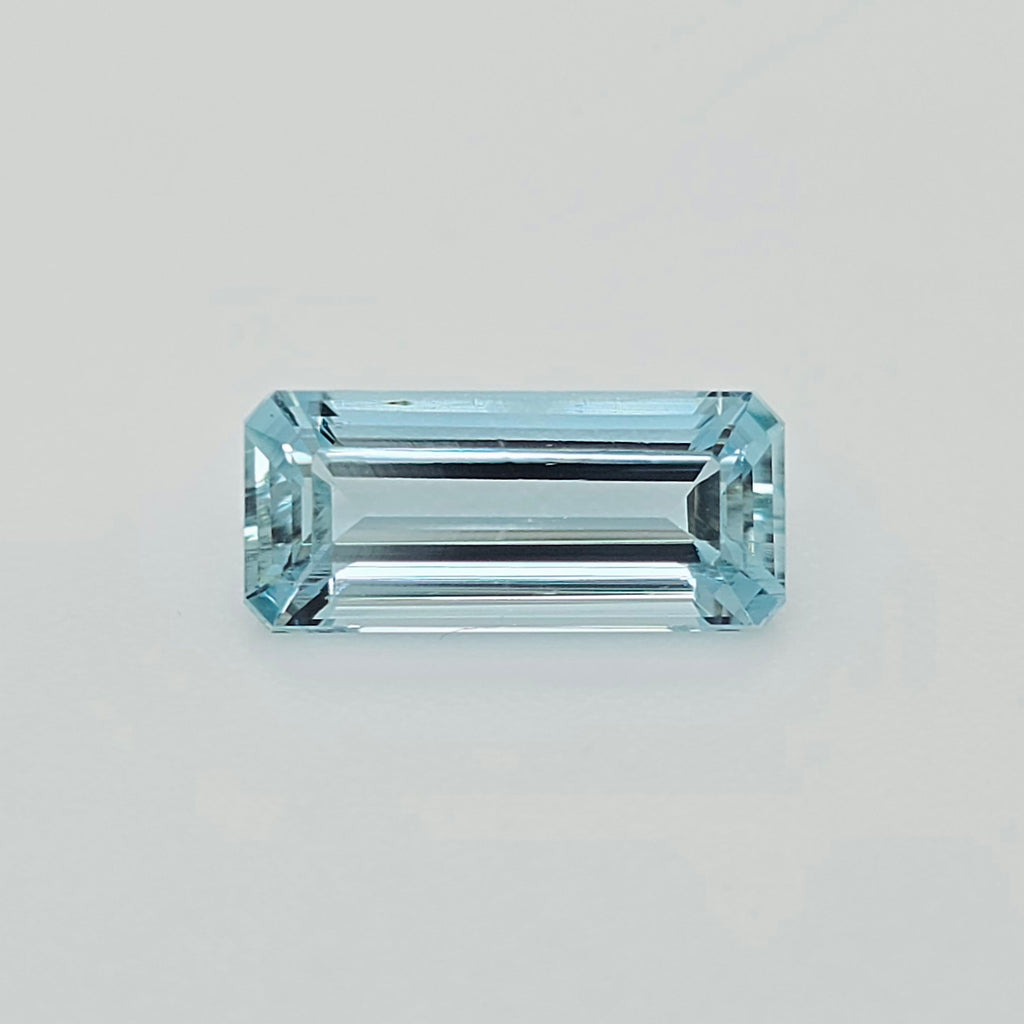 A rectangular emerald-cut light blue gemstone, centered on a clean, light gray background.