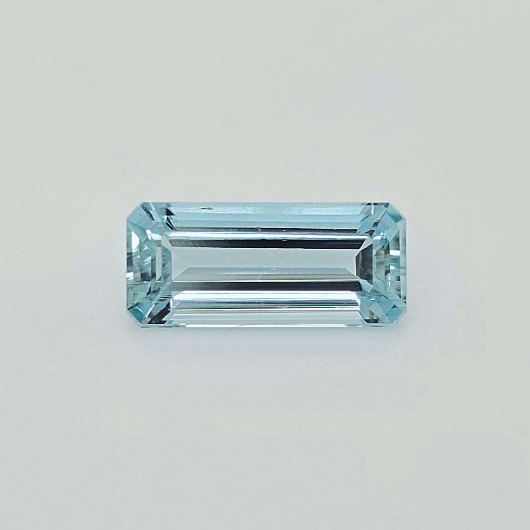 A rectangular emerald-cut light blue gemstone, centered on a clean, light gray background.