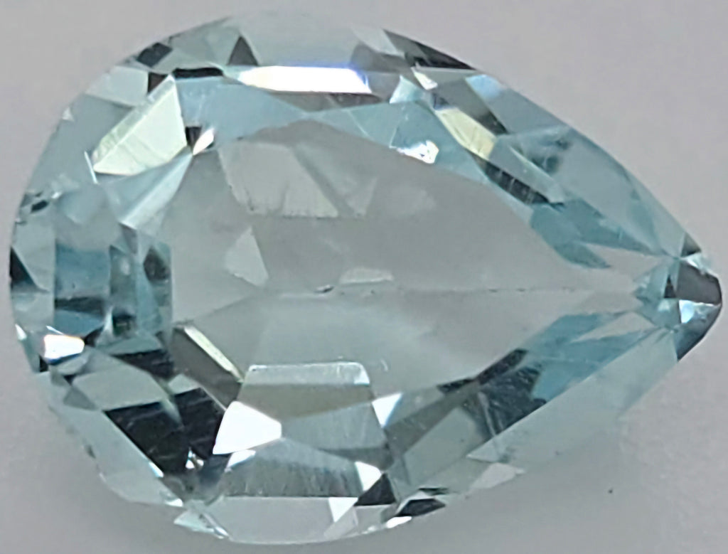 A faceted pear-cut light blue gemstone, shown in close-up against a neutral light gray background.