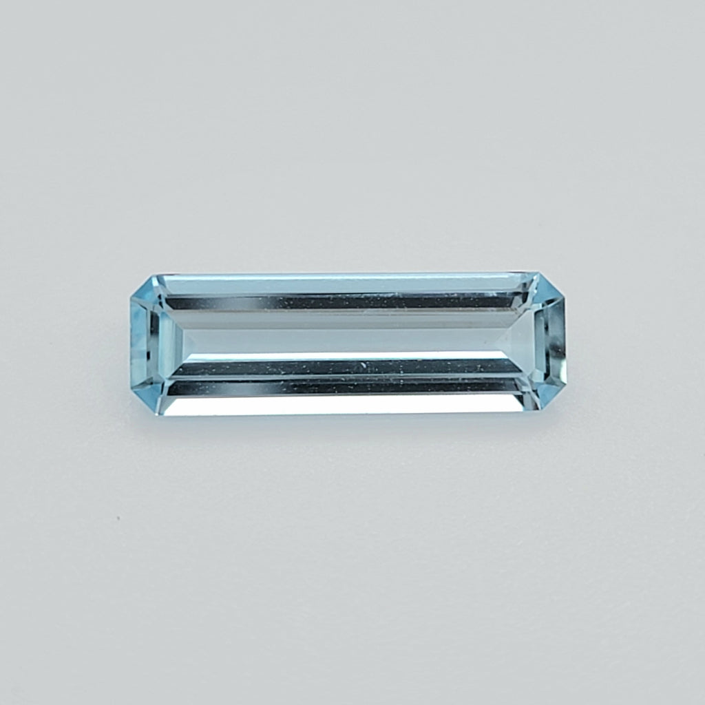 A rectangular emerald-cut light blue gemstone with a faceted, reflective surface, centered on a plain light gray background.