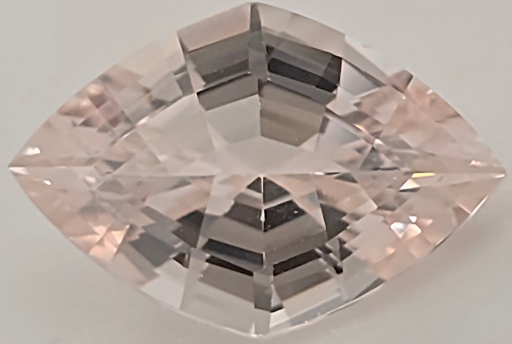 A lozenge cut pink gemstone with a faceted, clear appearance, centered on a light gray background.