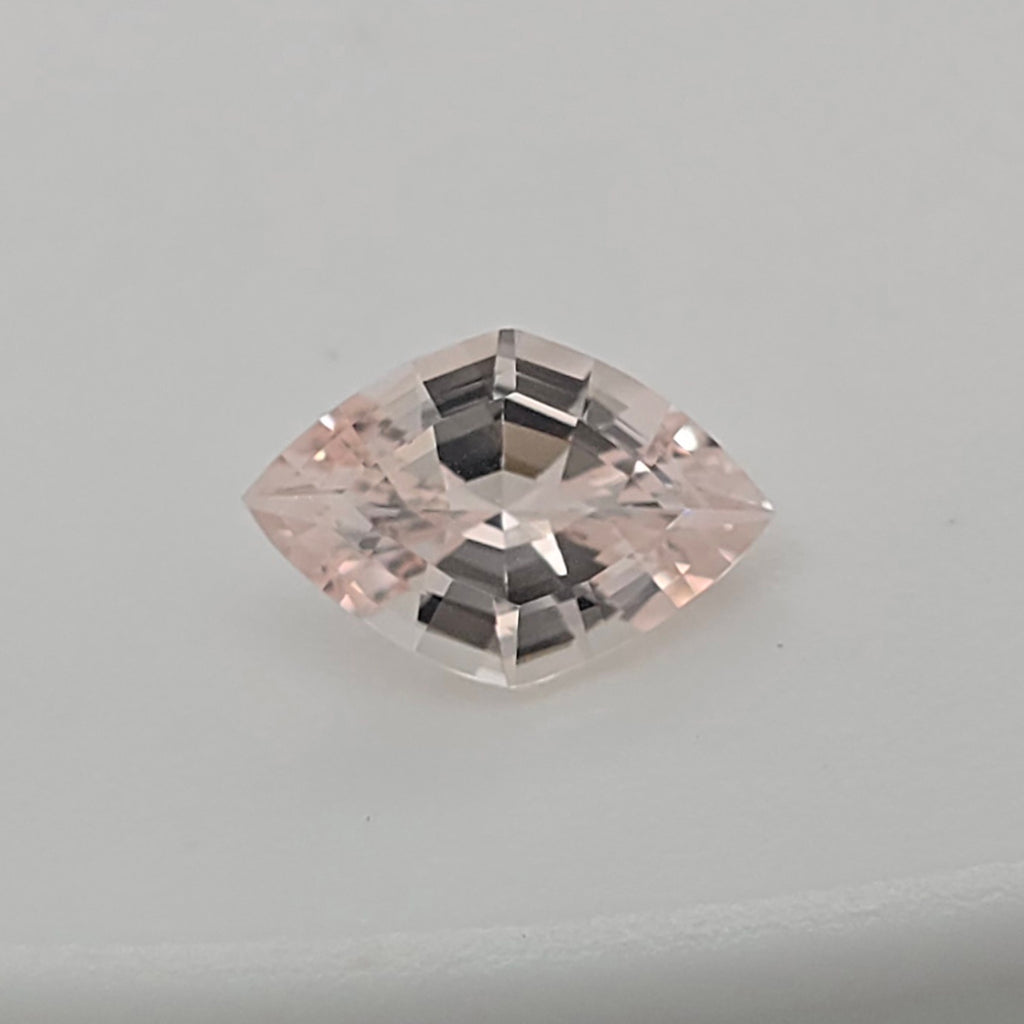 A single lozenge cut pink gemstone with a faceted, reflective surface, centered on a plain light gray background.