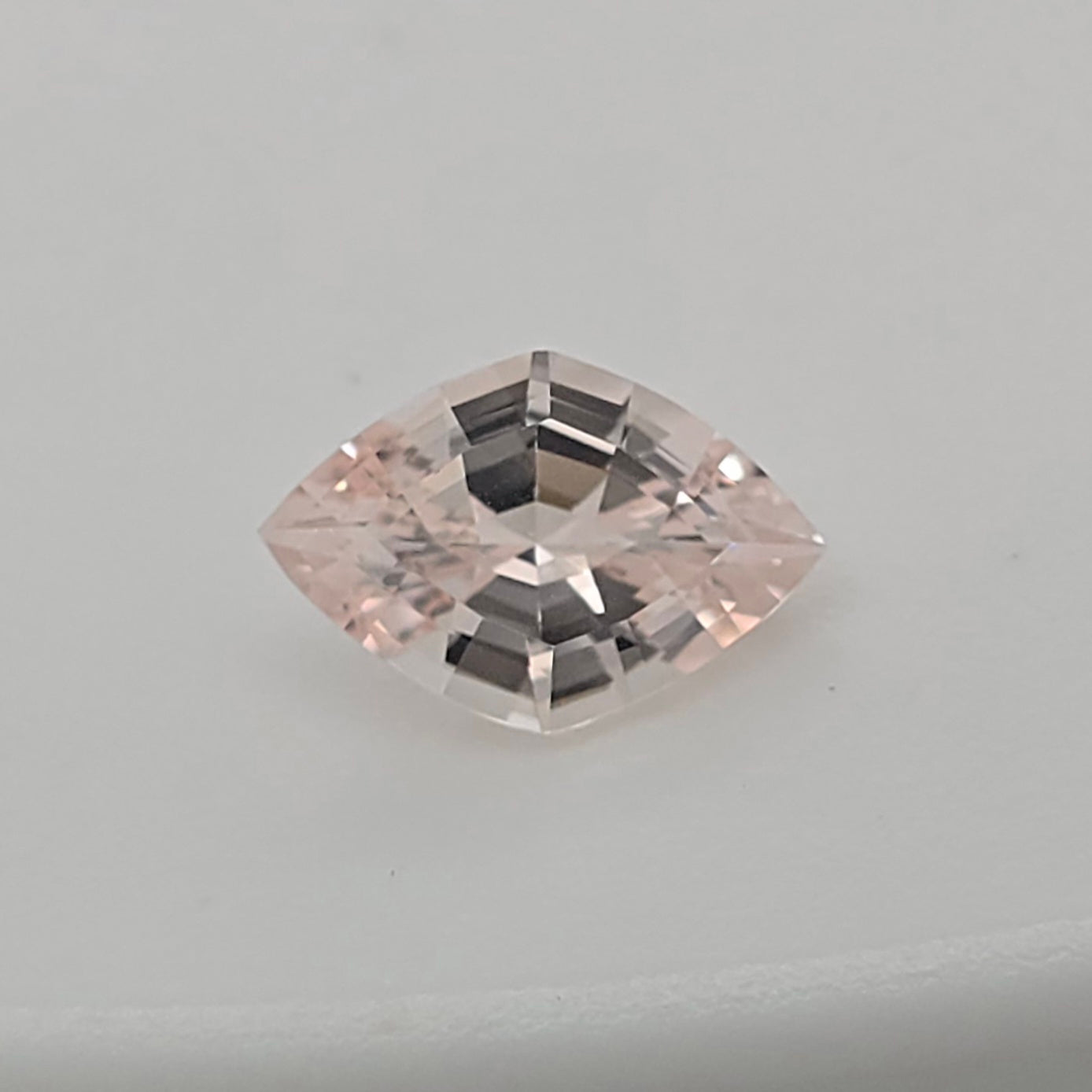 A single lozenge cut pink gemstone with a faceted, reflective surface, centered on a plain light gray background.