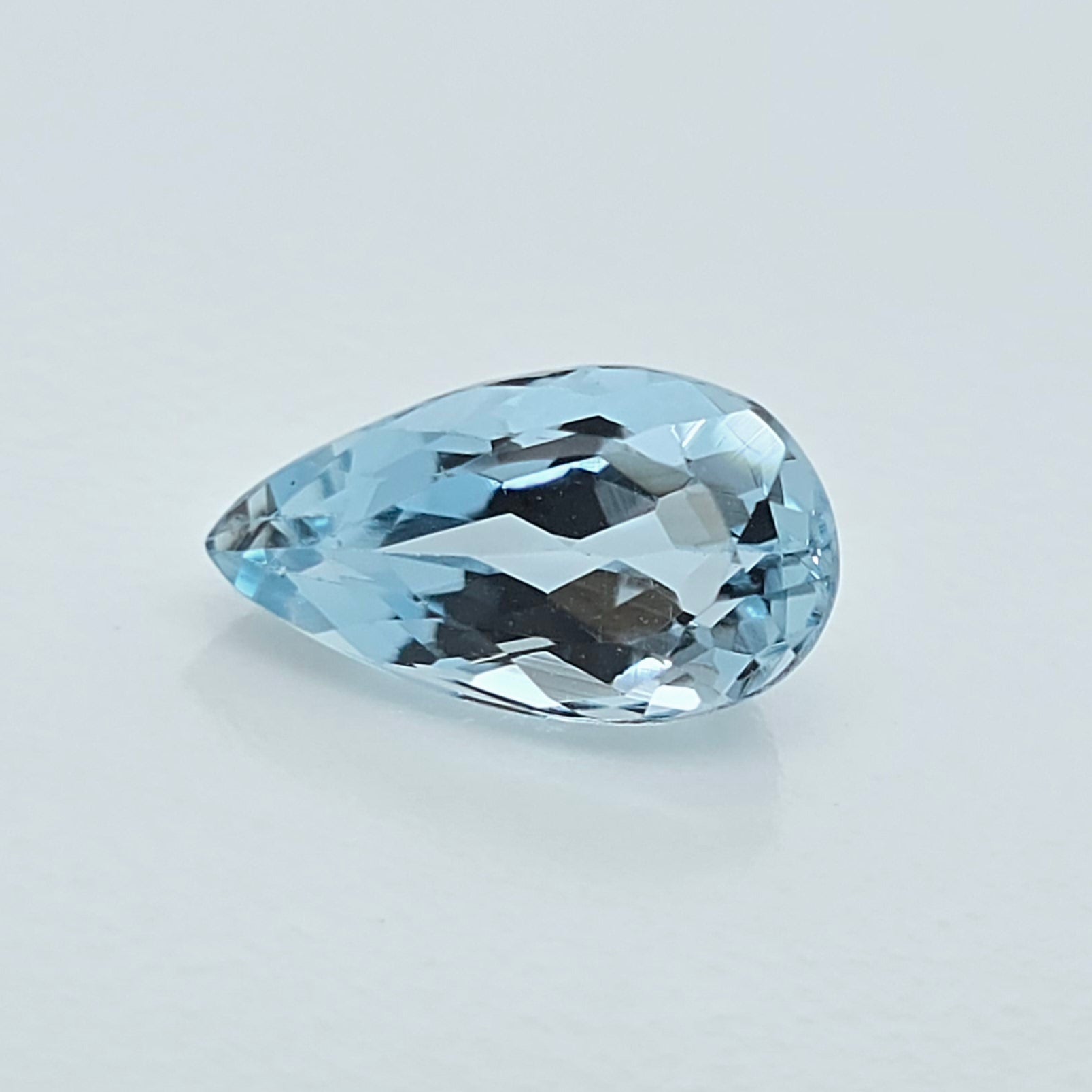 A single pear-shaped light blue gemstone with a faceted cut, displayed on a clean, light gray background.