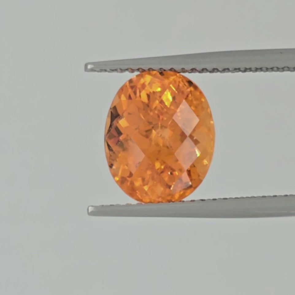 Video of a bright orange faceted stone being displayed in tweezers