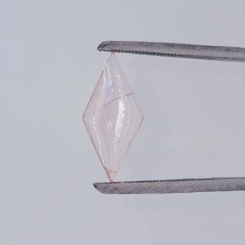 Video of a light pink diamond shaped gemstone with natural inclusions in tweezers against a white background