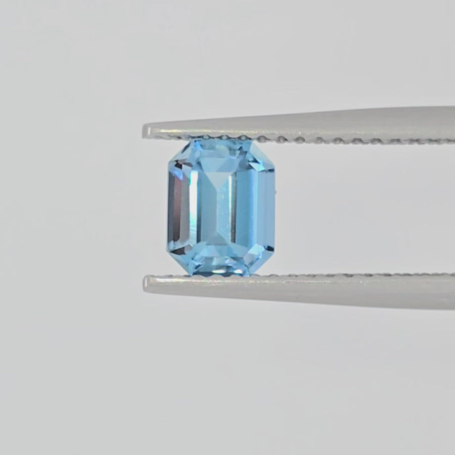 Video of an emerald cut light blue gemstone in tweezers against a white background
