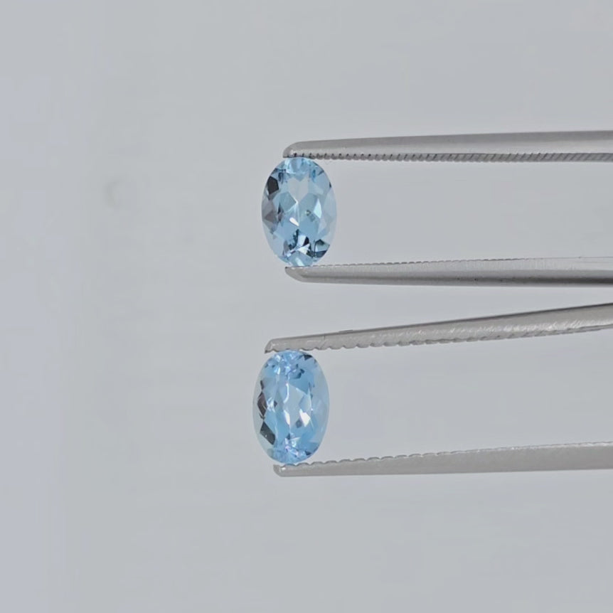 Video of two faceted oval gemstones in tweezers against a light background