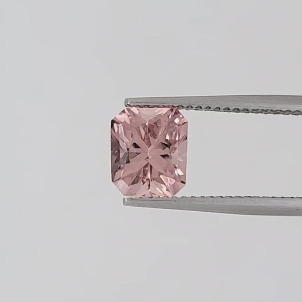 Video of a transparent, radiant cut pink gemstone in tweezers against a white background