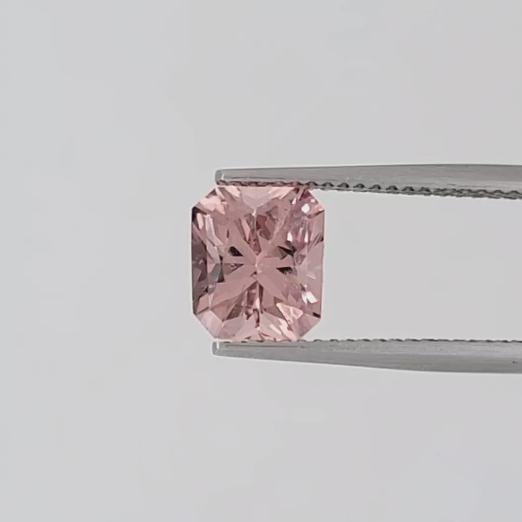 Video of a transparent, radiant cut pink gemstone in tweezers against a white background