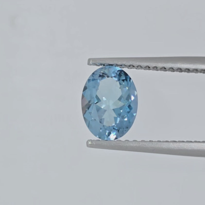 Video of a faceted blue gemstone in tweezers against a white background