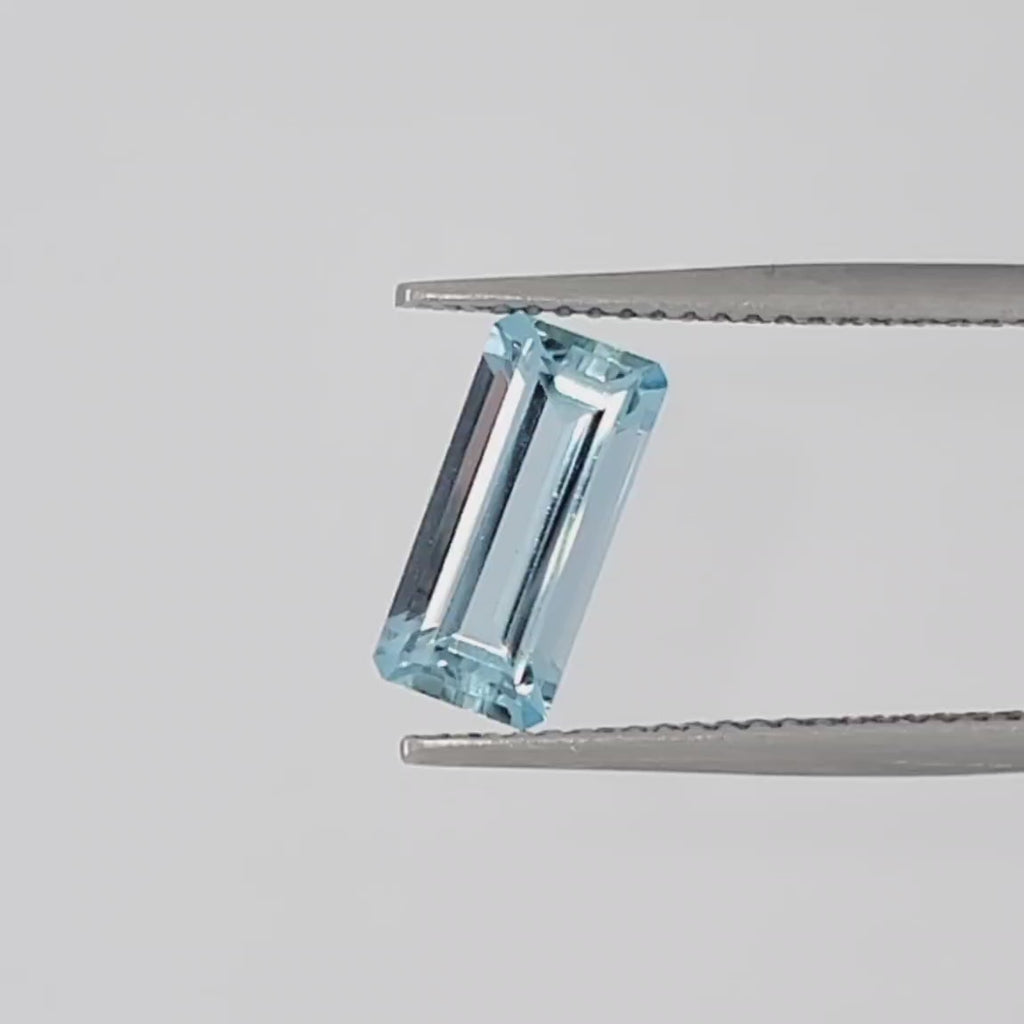Video of a faceted emerald cut gemstone in tweezers against a white background
