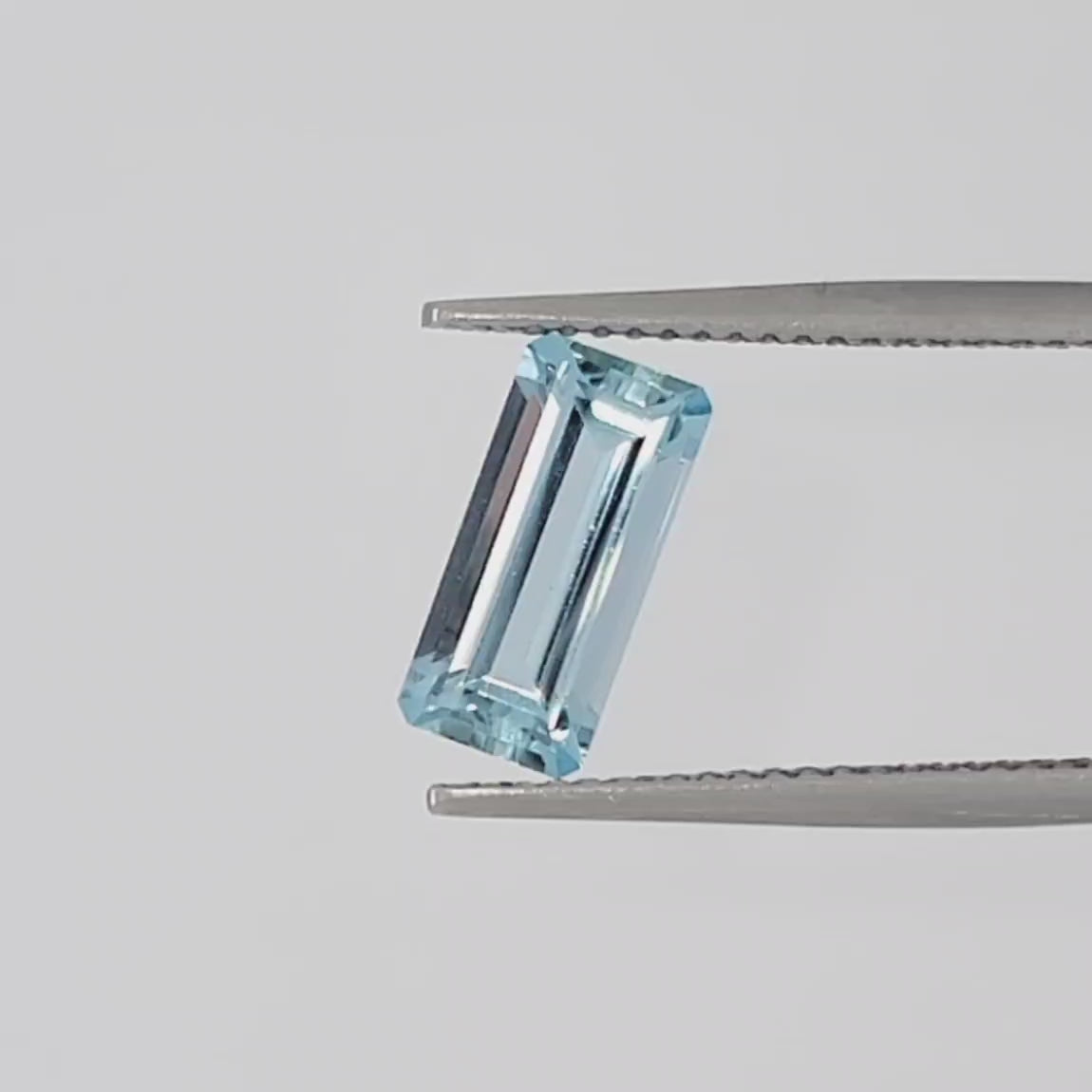 Video of a faceted emerald cut gemstone in tweezers against a white background