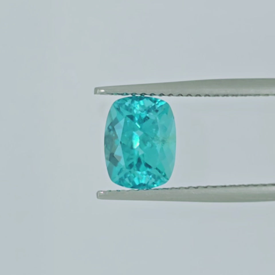 A video of a cushion-cut, faceted blue gemstone in tweezers, shown on a plain white background.