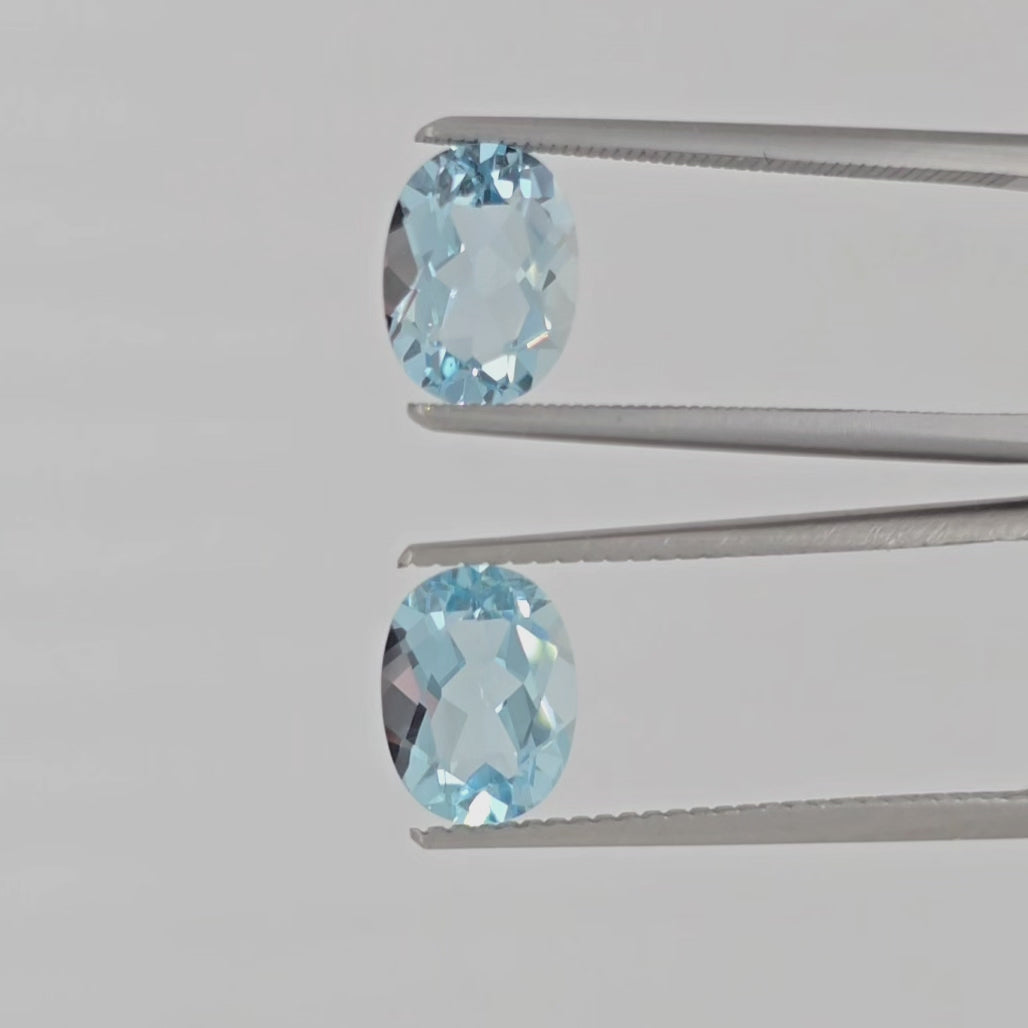 Video of a pair of oval faceted light blue gemstones in tweezers against a plain white background