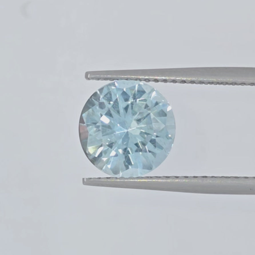 Video of a round light blue faceted gemstone in tweezers against a plain white background