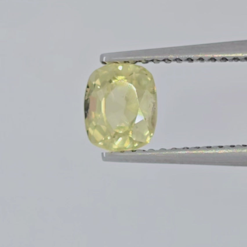 A video of a cushion-cut yellow gemstone with a faceted cushion shape, displayed in tweezers on a light gray background.