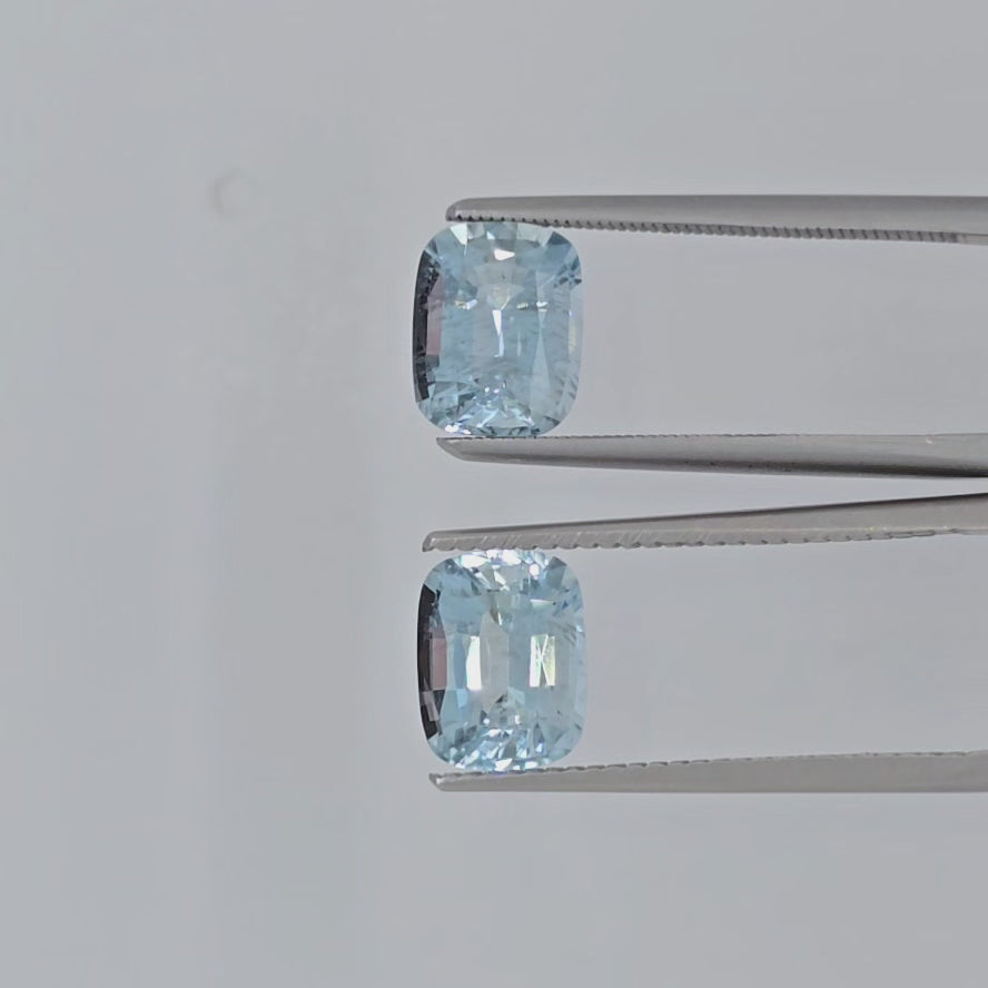 Video of two cushion cut light blue faceted stones in tweezers against a plain light gray background