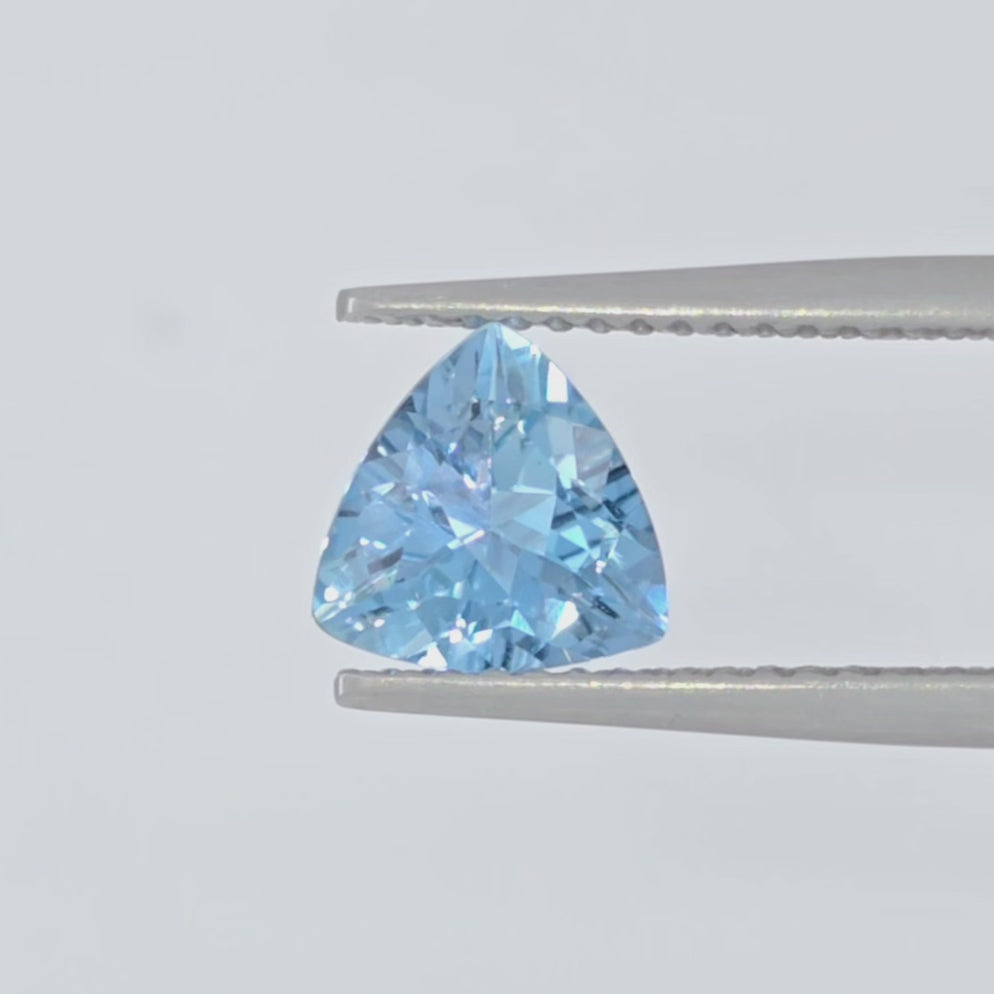 Video of a light blue triangular faceted gemstone in tweezers against a white background