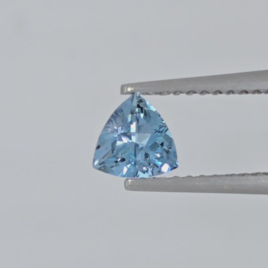 Video of a triangular cut blue gemstone in tweezers against a white background