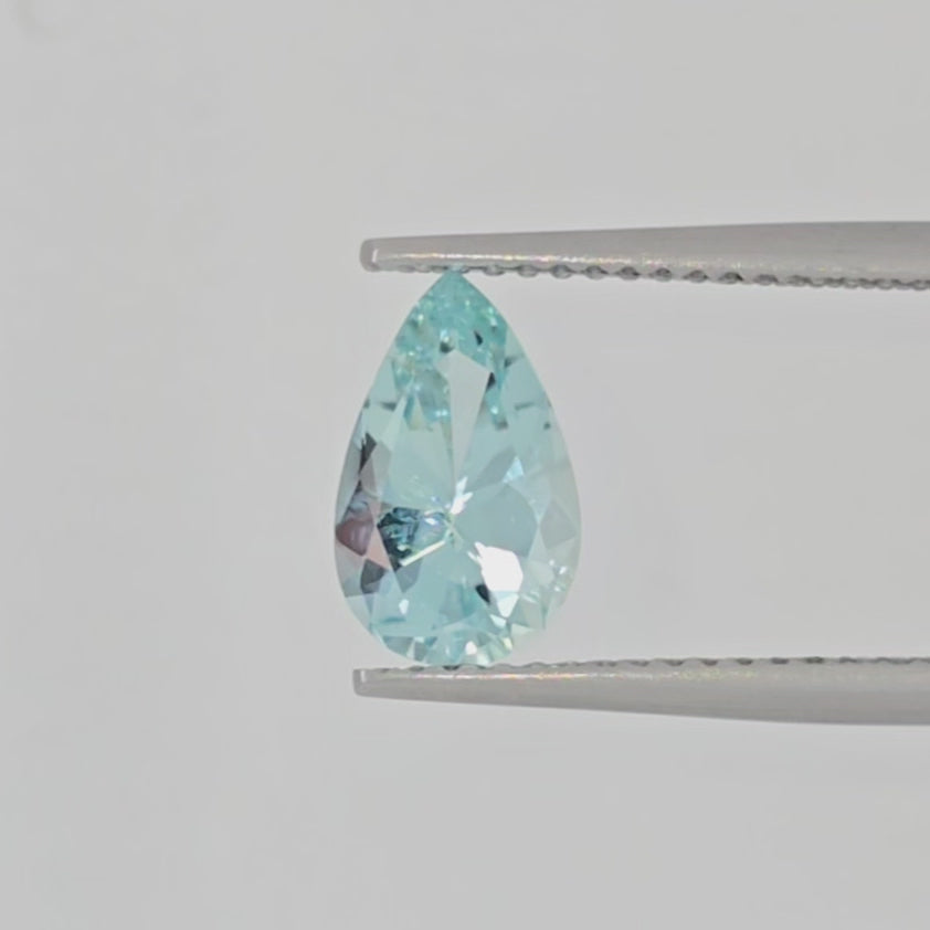 Video of a faceted light greenish blue pear shaped gemstone in tweezers against a white background
